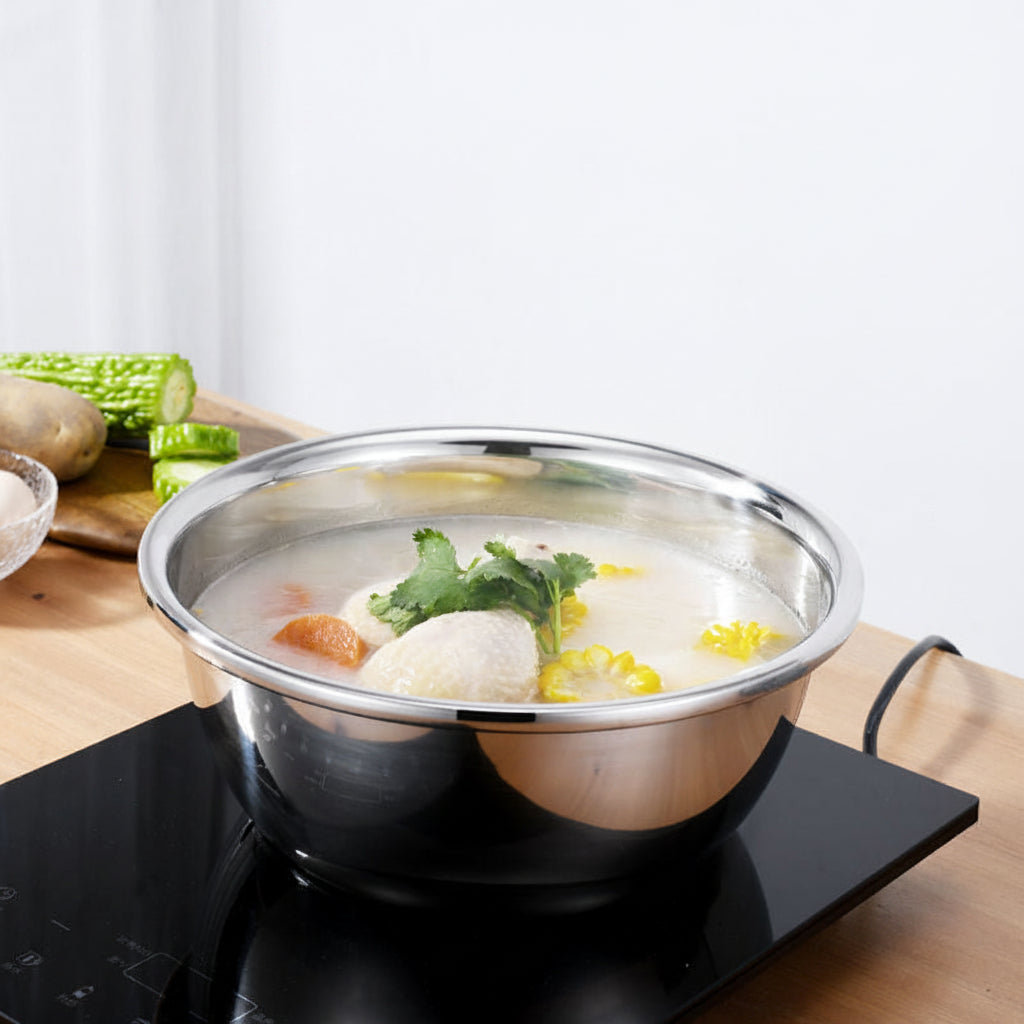 Stainless steel pot  basin with soup on an electric stove, surrounded by vegetables.